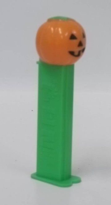 PEZ - Pumpkin (Version B) Dispenser, plastic Halloween-themed pumpkin candy dispenser with a jack-o'-lantern face and green base.