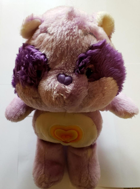 Care Bears Cousins - Bright Heart Raccoon, plush toy with a fluffy purple and tan fur body, purple heart-shaped nose, and purple yarn-like puffs on its cheeks, standing on a plain surface.