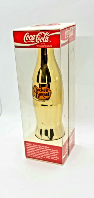 Coca-Cola Cracker Barrel Gold Coca-Cola Collector Bottle, gold-colored collectible Coca-Cola bottle in packaging.
