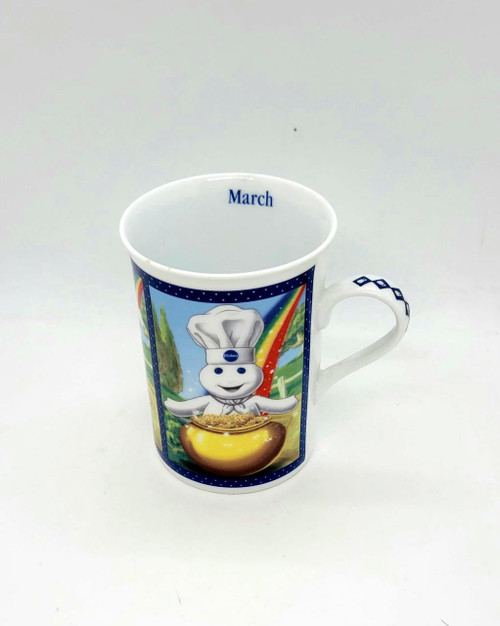 Pillsbury Doughboy Fine Porcelain Collector Mug: March St. Patrick's Day Wish, features a cheerful Pillsbury Doughboy dressed as a chef with a rainbow, green hills, and a pot of gold.