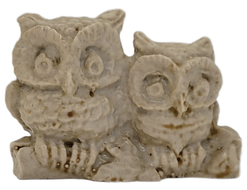 Two ivory resin owls sitting together on a woodland log