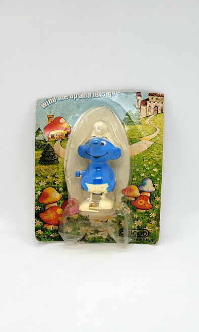 Smurfs Galoob Smurf Wind-up Toy, blue Smurf figurine with a big smile and white pants in transparent packaging with colorful mushroom and garden illustrations.