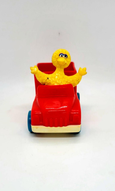 Sesame Street Big Bird Driving USPS Truck, toy figure of Big Bird sitting in a red toy truck with blue wheels.