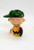 Peanuts Vintage 1950 Charlie Brown Finger Puppet, vintage toy figurine of Charlie Brown from Peanuts dressed in a yellow shirt with a black zigzag pattern, wearing a green cap, and holding a black baseball glove.