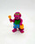 Barney and Friends 1993 Beach Barney PVC Toy Figure, colorful purple dinosaur toy with yellow sunglasses, green shirt, blue shorts with yellow stars, holding a yellow beach shovel and a yellow bucket.
