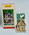 Lemax 95512 The Secret Santa Christmas Shoppe, detailed miniature holiday shop with snow-covered roof, green shingles, brick chimney, and festive decorations.