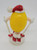 M&M's Candy Topper Ornament: Yellow M&M Skiing, featuring a yellow M&M character wearing a Santa hat and white gloves with red shoes, standing on a white base.