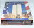 Master Pieces God Bless America: September 11, 2001 550 pc Jigsaw Puzzle, image of the puzzle box featuring a depiction of the World Trade Center with American flag graphics and Remembrance message.