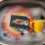 Stranger Things VHS Cassette Kitchen Sponges, vintage VHS tapes of Stranger Things series submerged in soapy water with yellow mug in the sink.