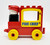 LEGO DUPLO 1985 2403 Fire Chief Building Set, a colorful toy fire truck with a red body, yellow wheels, a yellow window frame with 'FIRE CHIEF' text, and a black and white fire chief figurine with a red hat.