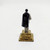 Unknown Vintage President Franklin Delano Roosevelt 2-inch Plastic Figure, back view of a miniature figurine of President Roosevelt dressed in a dark cape and light-colored suit, standing on a gold-colored base.