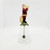 Novelino Inc. Novelino 1992 Christmas Thru The Ages Modern Santa Bell, a detailed decorative bell featuring a Santa Claus figure holding a letter, standing on a green base with a small holly charm hanging from the bell.