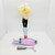 Monster High 2015 Surf to Turf Lagoona Blue Doll, loose doll with long blonde curly hair, wearing black pants and pink shoes, standing on a pink skateboard with teal wheels and a small scooter accessory in front on a white background.