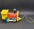 Vintage Fisher-Price 1964 #643 Toot-Toot Engine pull along toy. Wooden cut-out train engine with a rounded boiler that has red paper lithographs on the sides with a blue "sign" marked "Toot Toot" in white. The engine has a yellow plastic front grill and cowcatcher, a yellow plastic cab with a roof, a BLACK wooden smoke stack with small white squares on top, and 4 BLUE wooden wheels with white plastic pistons attached. When pulled, the pistons move and the engine makes a "chug-chug" sound. The model number is marked in small print by the cow catcher. Measures 6-1/4" long, 4-1/4" high, 3-1/4" wide.