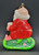Vintage Kurt S. Adler ceramic hanging Christmas Ornament of Santa sitting on green bench putting on his black boot. The ornament is 3.5-inches tall and 2.25" wide.