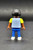 Geobra the German manufacture of Playmobil City Life School Bus black student 2-inch tall figure for ages 4+ from the 5940 City Life School Bus set. The figure is wearing a blue/grey striped shirt with yellow sleeves, blue pants and has black hair.