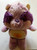 Care Bears Cousins - Bright Heart Raccoon, plush toy with a fluffy purple and tan fur body, purple heart-shaped nose, and purple yarn-like puffs on its cheeks, standing on a plain surface.
