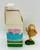 AVON Somersaults Zippy Mini Doll, a small rubber figure of a humorous character with a textured, peanut-like body, pink tongue, and wearing pink and white shoes, standing on a green base next to its white packaging box with colorful text and fencing illustration.