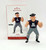Hallmark Keepsake Ornament The Goonies Sloth, a detailed 3D figurine of Sloth from The Goonies dressed in a black hat, gray pants with patches, and a black T-shirt with 'Hey You Guys!' written on it, standing next to its packaging.