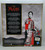 Disney Mulan Two Reflections Set Doll, image showing the back of the doll featuring her in traditional armor holding a sword, with Chinese mountain landscape background.
