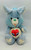 Care Bears Cousins - Swift Heart Rabbit plush toy, soft light blue stuffed animal with large ears, green heart-shaped nose, embroidered red heart with angel wings on its belly, and matching heart patches on its feet.