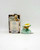 Cherished Teddies 2001 Cherished Teddies #873349 Teal Spring Bonnet Figurine, a small teddy bear in a floral bonnet with a green ribbon, displayed alongside its original packaging on a plain white background.
