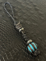 Handmade Turquoise Orbital Bead Knife Lanyard with Black Samurai Mask, Hematite Accents, and Black Metal Column Bead on Reflective Black Paracord