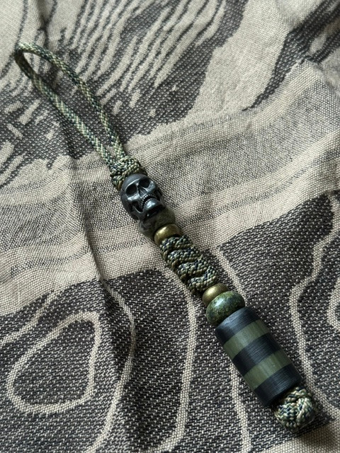 Jungle Camo Paracord Tactical Style Knife Lanyard with Black Carbon Fiber and OD Green G10 Bead, Black Metal Skull Bead, and Brass Accents
