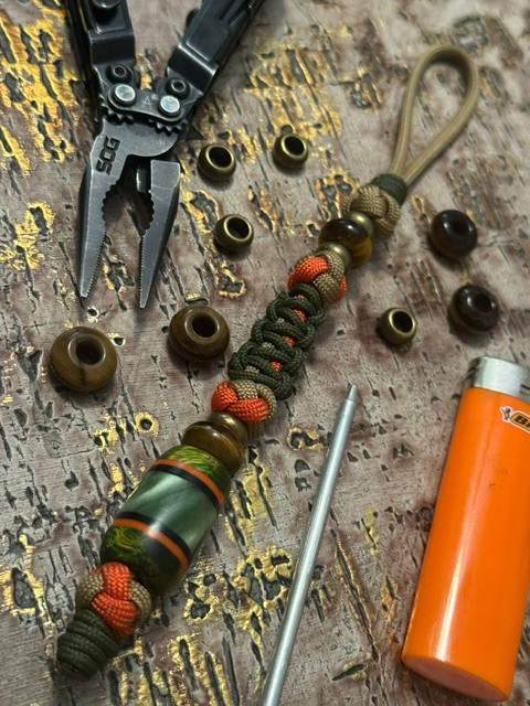 Coyote Tan, Hunter Orange, and OD Green Paracord Knife Lanyard with Dyed Burl, Black G10, Orange G10, and Green "Swamp" Resin Bead Accented by Brass & Tiger's Eye