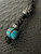 Handmade Turquoise Orbital Bead Knife Lanyard with Black Samurai Mask, Hematite Accents, and Black Metal Column Bead on Reflective Black Paracord