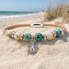 Cork bracelet with green and cream ceramic beads and sterling silver turtle charm displayed on driftwood on the beach - Crabby Mermaid