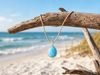 Larimar teardrop pendant necklace on cork cord hanging from driftwood with ocean view - genuine Dominican Republic Larimar - Crabby Mermaid