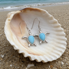 Larimar turtle dangle earrings displayed in a clam shell on the beach — genuine Dominican Republic Larimar — Crabby Mermai