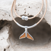 Koa wood whale tail pendant on cork cord displayed on pale driftwood - Crabby Mermaid