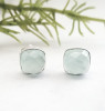 Pair of aqua chalcedony cushion stud earrings on white background with greenery — faceted natural gemstone in .925 sterling silver