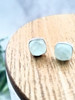 Aqua chalcedony cushion stud earrings in sterling silver displayed on wood surface — soft pale aqua gemstone studs