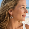 Woman wearing sterling silver sea turtle dangle earrings with Hawaiian koa wood inlay on a Florida beach - Crabby Mermaid