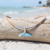 Larimar whale tail cork necklace on driftwood with palm trees and ocean in the background