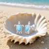 Larimar turtle stud earrings displayed in an open seashell on the sand — Crabby Mermaid