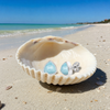 Larimar trillion stud earrings resting in a clam shell on a Florida Gulf Coast beach