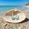 Larimar square drop earrings resting in a clam shell on a Florida Gulf Coast beach