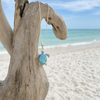 Larimar sea turtle necklace in sterling silver displayed on driftwood at the beach - genuine Dominican Republic Larimar - Crabby Mermaid