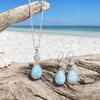 Larimar and cubic zirconia teardrop necklace and earring set in sterling silver displayed on driftwood at Florida Gulf Coast beach — genuine Dominican Republic Larimar — Crabby Mermaid