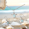Larimar sea turtle necklace and earring set in sterling silver styled on beach with seashells — genuine natural Larimar gemstone