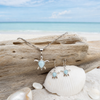 Larimar sea turtle necklace and earring set displayed on driftwood with shell and turquoise ocean in background — genuine Dominican Republic Larimar — Crabby Mermaid