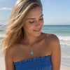 Sandy blonde model wearing Larimar dolphin teardrop necklace in sterling silver at Florida Gulf Coast beach — genuine Dominican Republic Larimar — Crabby Mermaid