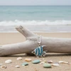 Aqua crystal angel fish pendant necklace resting on driftwood with shells and sea glass on beach sand - coastal jewelry - Crabby Mermaid