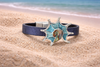 Blue abalone conch shell magnetic bracelet with navy band resting in beach sand with ocean waves in background - coastal jewelry - Crabby Mermaid