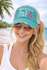 Woman at the beach wearing teal Beach Hair Don't Care trucker hat with pink anchor graphic and tan mesh back — Crabby Mermaid