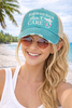 Woman at the beach wearing teal Mermaid Hair Don't Care trucker hat with distressed finish and mesh back - Crabby Mermaid